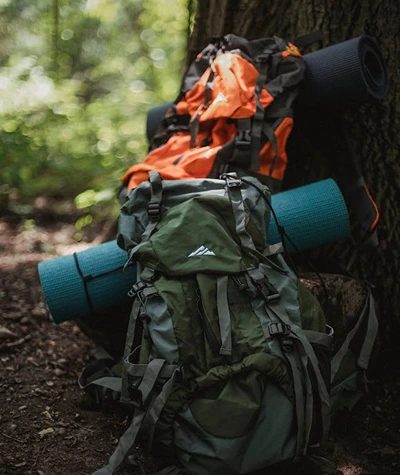 Beginner overnight backpacking gear layout with backpack, tent, sleeping bag, sleeping pad, stove, water filter, food canister, and headlamp