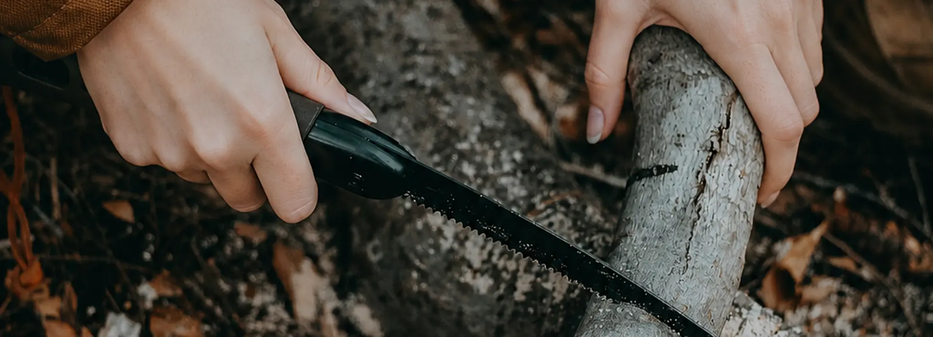Folding saw, bow saw, and pocket chainsaw arranged with small logs and kindling on an outdoor wooden surface