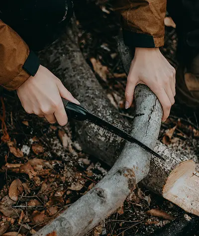 Folding saw, bow saw, and pocket chainsaw arranged with small logs and kindling on an outdoor wooden surface