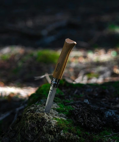 Camping knife with sheath, cord, kindling, and simple camp supplies arranged on a wooden outdoor table